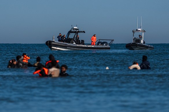 Los barcos de la policía franceses observan mientras los migrantes entran en el mar para abordar los inflables que esperan que los lleven a Inglaterra.
