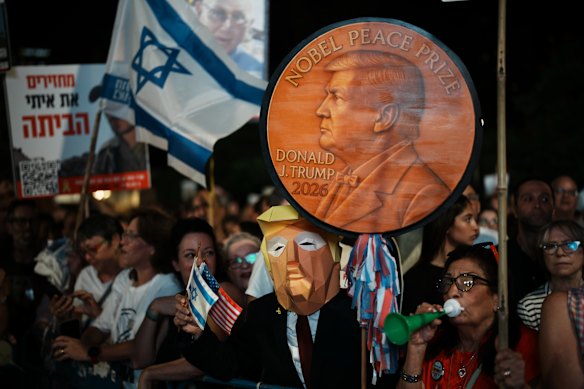 Un hombre con una máscara de Donald Trump sostiene un cartel que respalda al presidente estadounidense para el Premio Nobel de la Paz en Tel Aviv.