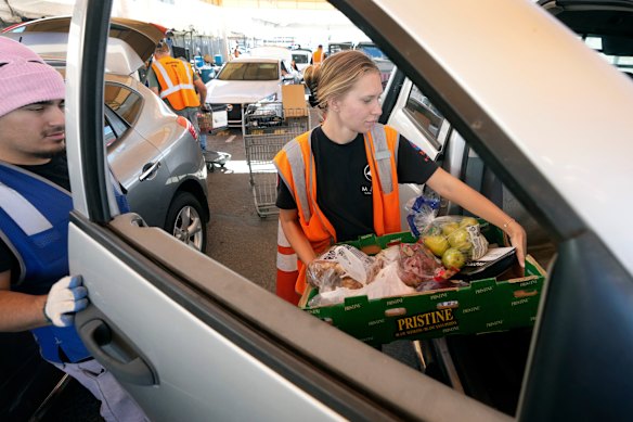 Josh Torres, empleado del St Mary's Food Bank of Arizona, y la voluntaria Kayli Iverson entregan comida a un automóvil en las instalaciones principales de Phoenix el martes.